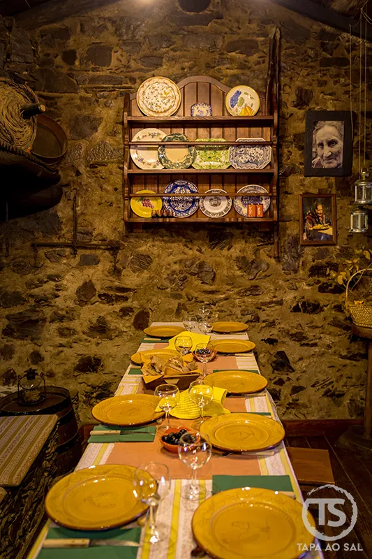 Sala rústica de restaurante no Talasnal com mesa posta para grupo em ambiente de pedra e serra