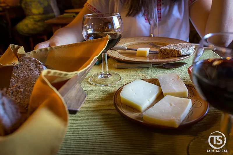 Mesa posta em restaurante no Talasnal com pão, queijo e vinho em ambiente rústico