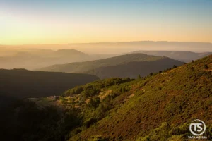 Paisagem ampla da Serra da Lousã ao entardecer, com encostas e vales em camadas