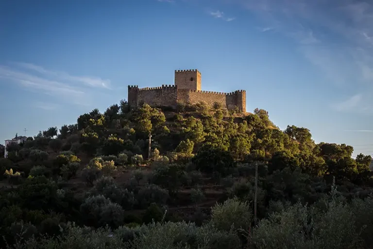 Castelo de Belver ao entardecer, visto do sopé da colina com vegetação mediterrânica