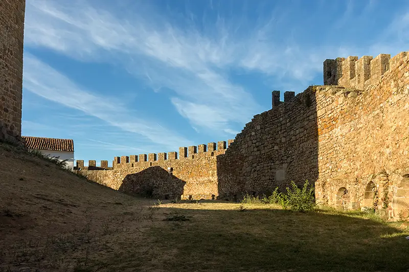 Interior das muralhas do Castelo de Belver com sombra e luz sobre a pedra antiga