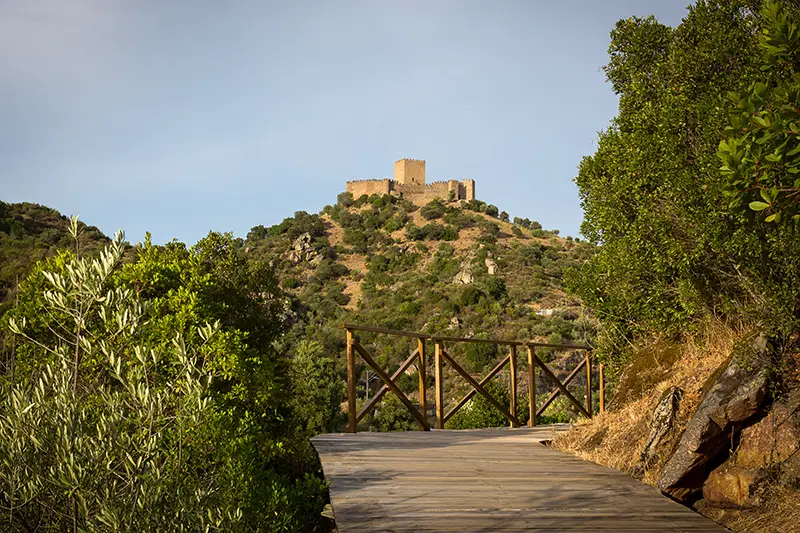 Vista do passadiço do Alamal com o Castelo de Belver ao fundo, sobre uma colina verdejante