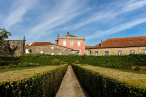 Jardim formal com sebes geométricas e edifício senhorial no centro de Santar Vila Jardim, em dia claro com céu azul.