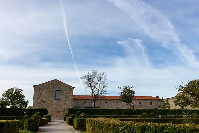 Jardins formais e edifício em pedra do projeto Santar Vila Jardim com céu limpo ao fundo