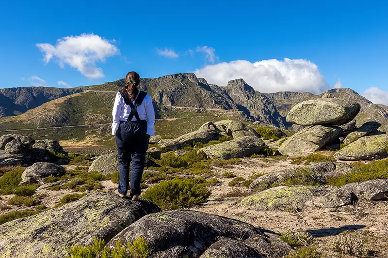 Mulher a contemplar a paisagem da Serra da Estrela entre blocos graníticos e montanhas ao fundo