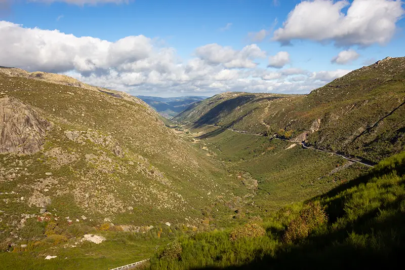 Vista aérea do Vale Glaciar do Zêzere na Serra da Estrela, com estrada sinuosa e montanhas verdes