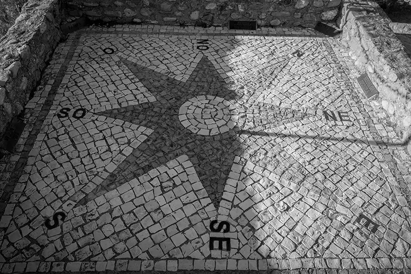 Imagem a preto e branco de uma rosa dos ventos em calçada portuguesa, situada no Centro Geodésico de Portugal em Vila de Rei.