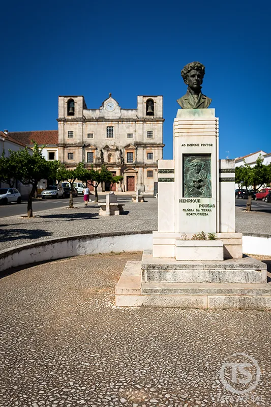 Estátua de Henrique Pousão na praça central de Vila Viçosa com a Igreja de São Bartolomeu ao fundo