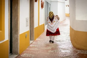 Nisa o que visitar – mulher com traje tradicional caminha por rua típica da vila, com casas alentejanas e chão empedrado.