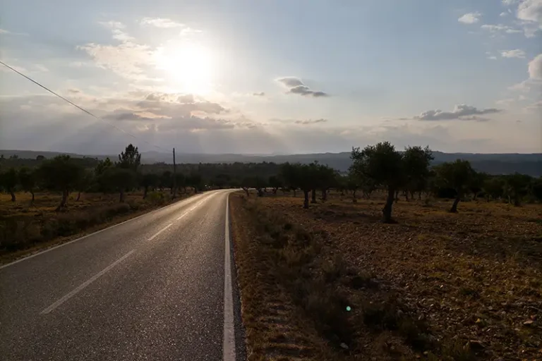 Estrada rural no Alto Alentejo com paisagem aberta e o sol a brilhar de frente, capturando a essência de um percurso de ciclismo no Alto Alentejo.