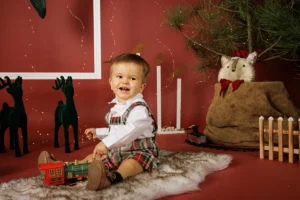 Criança sorridente durante uma sessão de fotografia escolar com tema natalício, capturada num cenário festivo.