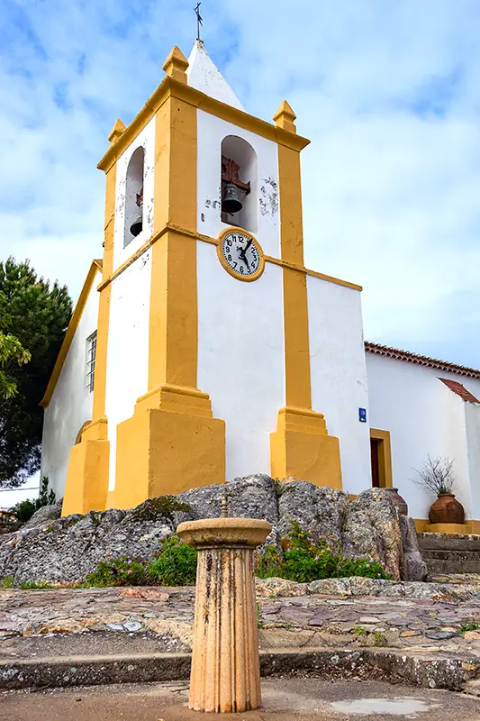 Torre sineira branca e amarela da igreja de Alter Pedroso, erguida sobre afloramento rochoso no Alentejo — paragem ideal num roteiro rápido para quem procura o que visitar em Portugal.