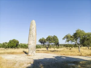 Menir da Meada ao entardecer, rodeado por paisagem natural alentejana com azinheiras e céu limpo