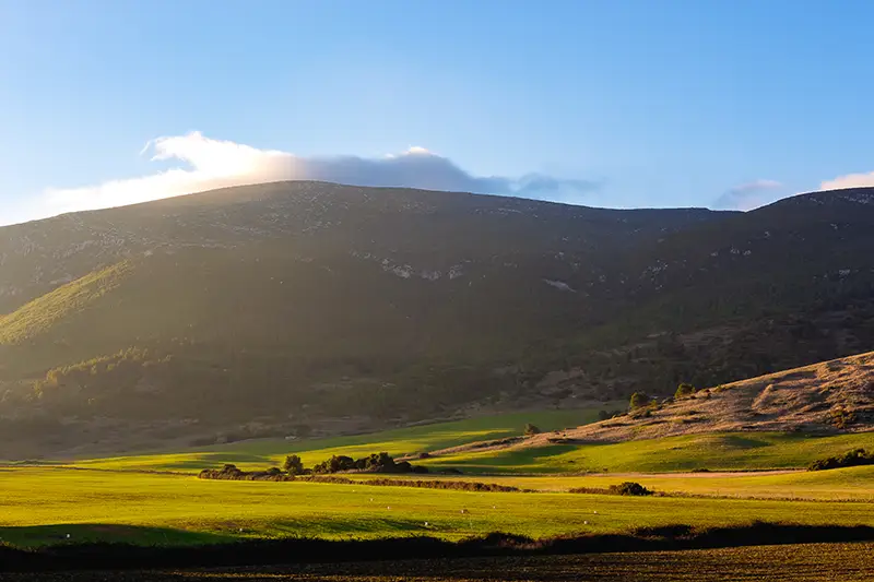 Luz dourada de fim de dia sobre a Serra de Montejunto, com campos verdes a perder de vista — paisagem natural que não podes perder ao explorar o que visitar em Portugal.