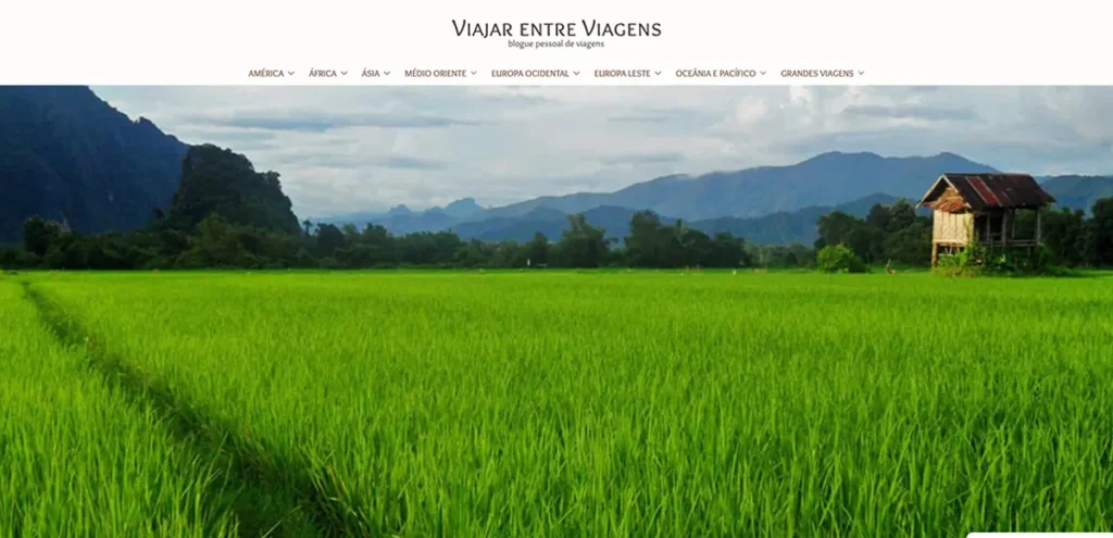 Captura de ecrã da homepage do blog Viajar entre Viagens com destaque para paisagem rural exuberante e casa de madeira sobre um campo verde.