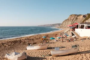 Praia de Porto Dinheiro ao final da tarde com barcos de pesca na areia, mar calmo e falésias ao fundo
