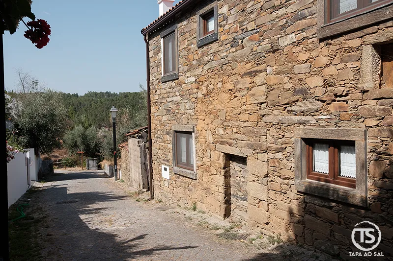Rua estreita e casas de xisto na Aldeia da Figueira com vista para a serra
