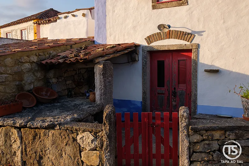Porta vermelha e pátio rústico em pedra na Aldeia da Mata Pequena