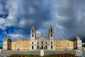 Fachada imponente do Palácio Nacional de Mafra com céu nublado dramático.