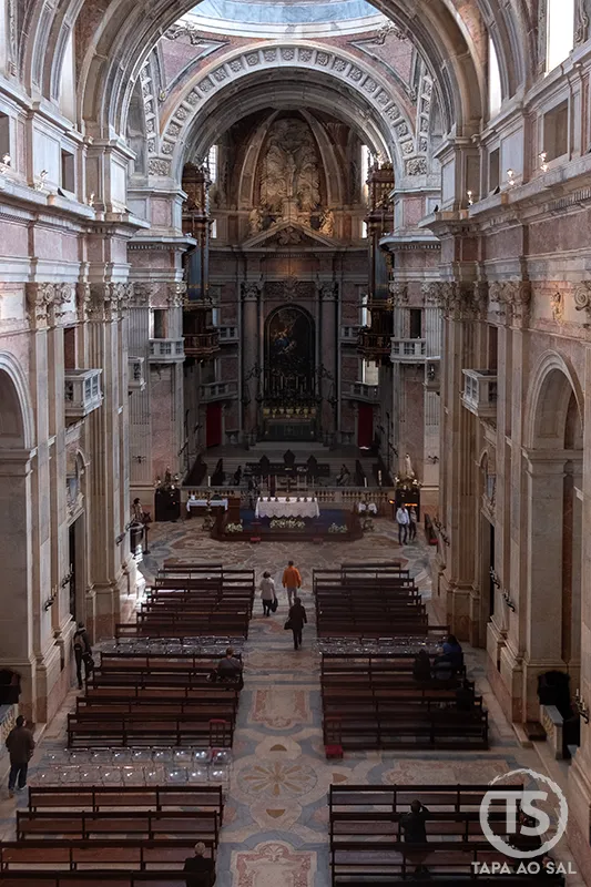 Interior da basílica do Palácio Nacional de Mafra com nave central e altar barroco iluminado