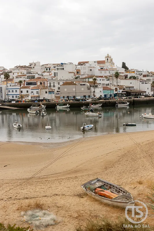 Barcos ancorados na maré baixa com vista para o centro histórico de Ferragudo