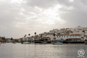 Casario branco de Ferragudo refletido no rio Arade sob céu nublado