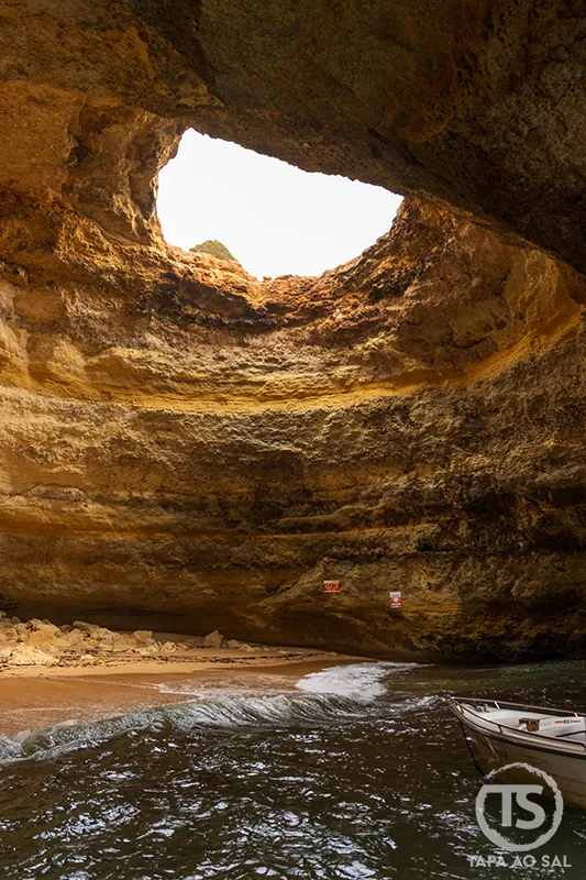 interior iluminado das Grutas de Benagil com barco e praia de areia dourada