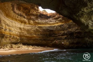 interior das Grutas de Benagil com praia de areia dourada e luz natural a entrar pelo teto