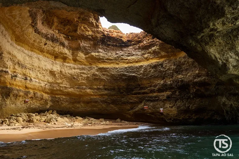 interior das Grutas de Benagil com praia de areia dourada e luz natural a entrar pelo teto