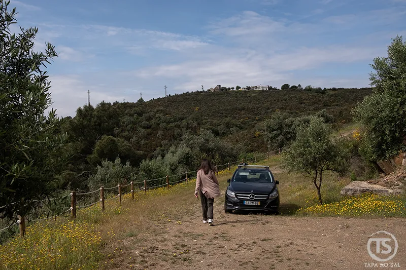 Pessoa a caminhar numa estrada rural junto a um carro no interior de Portugal, evocando alugar carro em Portugal para explorar paisagens naturais