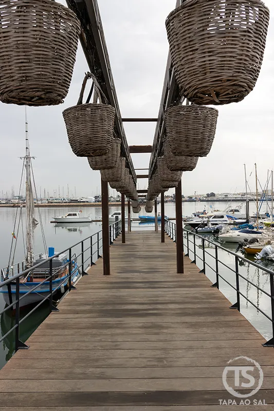 Passadiço de madeira na marina de Portimão com barcos e cestos de pesca suspensos, ponto típico a visitar em Portimão