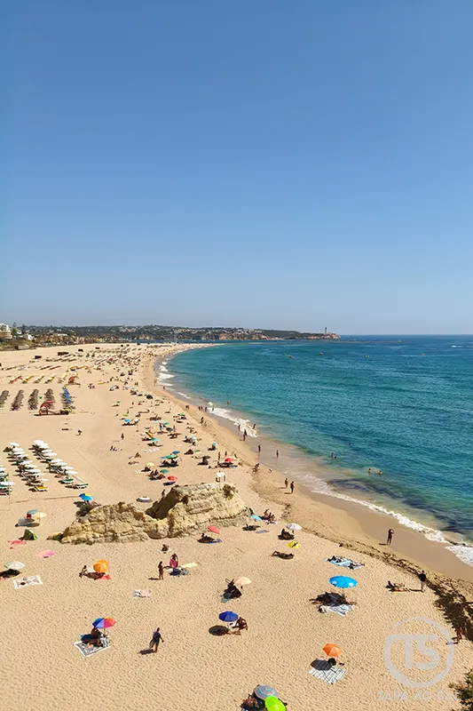 Praia da Rocha em Portimão vista ampla do areal dourado, mar azul e banhistas, um dos principais locais a visitar em Portimão