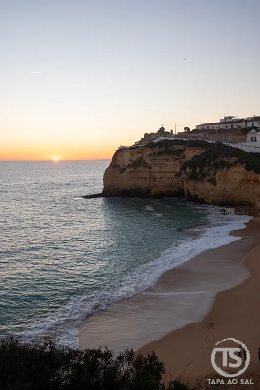 Pôr do sol sobre falésia e praia no Algarve, com luz dourada a cair sobre a costa junto ao mar