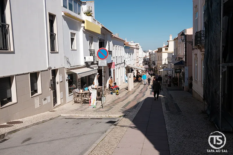 Rua do centro histórico de Lagos com casas brancas, comércio local e calçada portuguesa