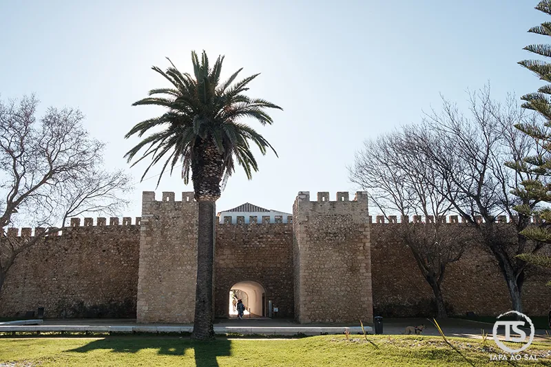 Muralhas do centro histórico de Lagos com arco de entrada e palmeira ao entardecer, Algarve