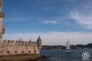 Torre de Belém junto ao Tejo em Lisboa, com veleiro a passar e céu amplo sobre a frente ribeirinha