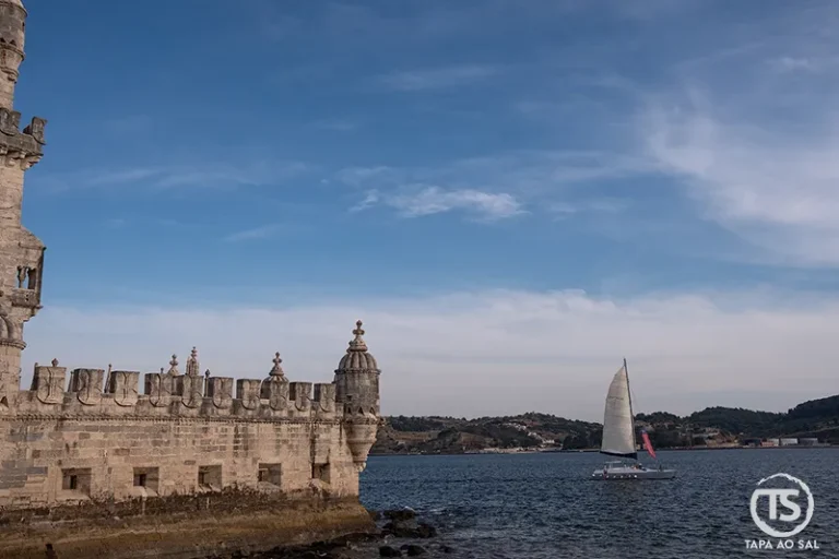 Torre de Belém junto ao Tejo em Lisboa, com veleiro a passar e céu amplo sobre a frente ribeirinha